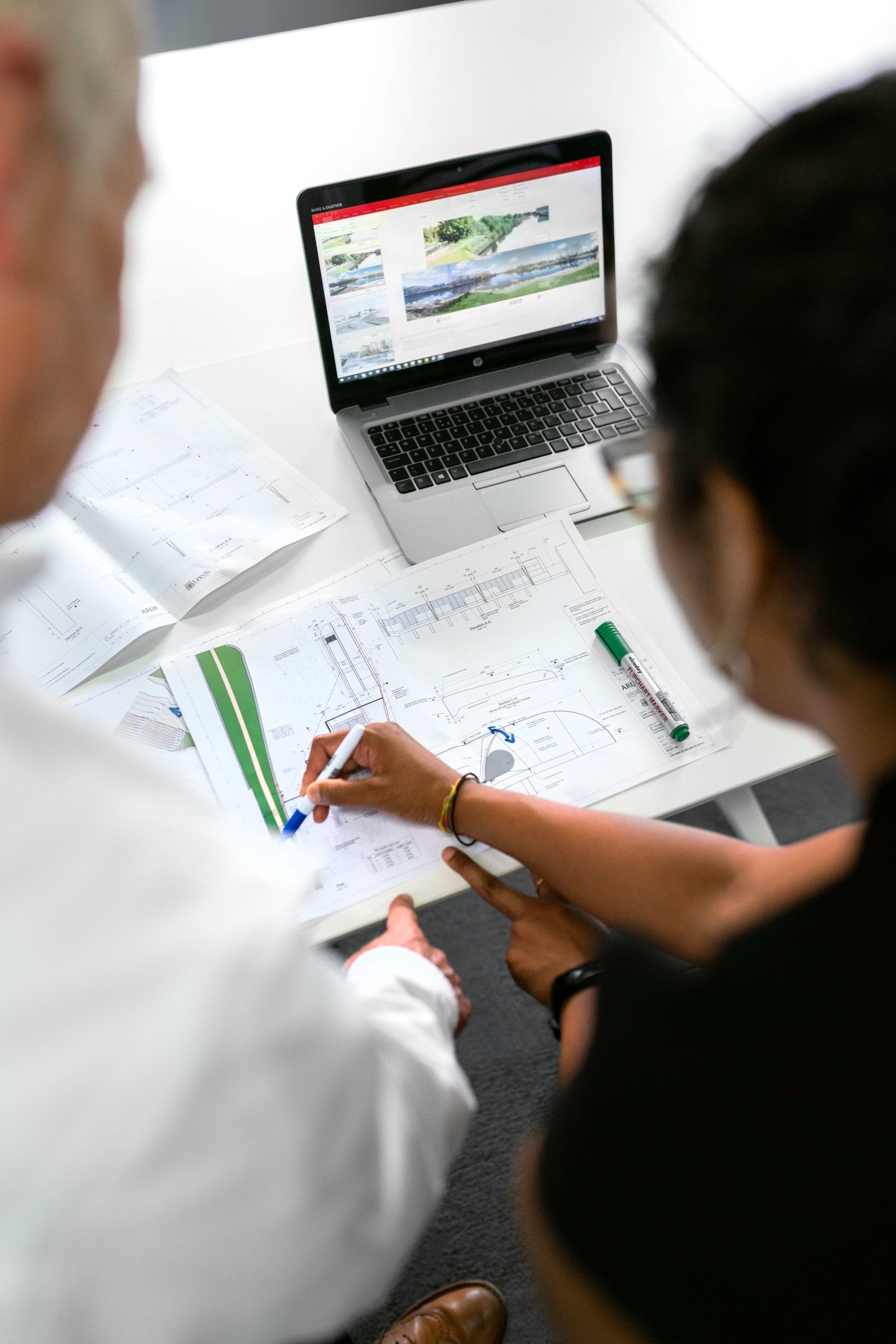 Two people reviewing drawings and information on a laptop